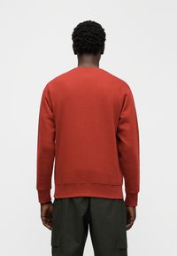 Sweatshirt vermelha com gola redonda, punhos e bainha canelados. Feita de um tecido macio, apresenta um design simples sem padrões ou detalhes.