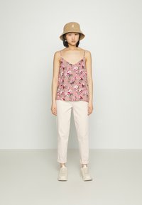 Top de alças spaghetti rosa floral combinado com calças claras arregaçadas e ténis bege, exibido contra um fundo neutro.