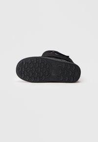 Sola preta de bota com padrão de piso oval e nome da marca "Love Moschino" visível, fotografada contra um fundo branco simples.