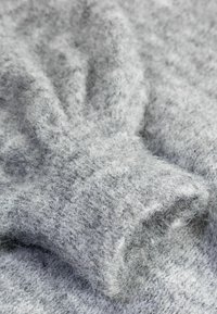 Gros plan d’un pull tricoté doux et duveteux gris clair montrant la texture et les détails du tissu et du poignet de la manche.