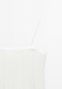 Haut sans manches blanc avec des fines bretelles, présentant un tissu texturé et des plis verticaux le long du corsage, mettant en valeur son design fluide.