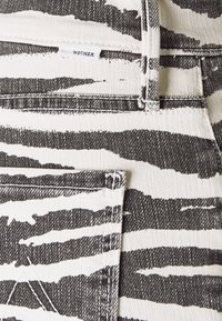 Tejido de mezclilla blanca con rayas de cebra negras. Presenta una pequeña etiqueta etiquetada como "MOTHER" y costuras visibles a lo largo del bolsillo y las costuras.