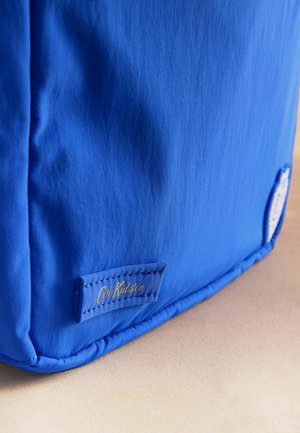 Helle blaue Stofftaschenecke mit Cath Kidston-Logoetikett, in goldenen Buchstaben auf einer beigen Oberfläche aufgenäht.