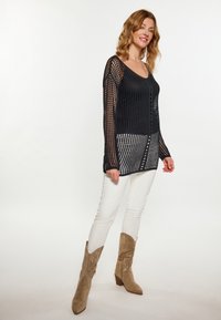 Zwart opengewerkt pullover met lange mouwen en een V-hals, gecombineerd met witte broek en beige cowboylaarzen. Getextureerd, lichtgewicht materiaal.