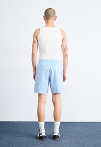 Shorts bleu deschis cu talie elastică, un top alb fără mâneci, șosete albe până la glezne și adidași negri. Design curat, minimalistic.