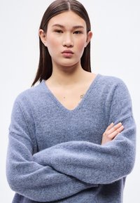 Ανοιχτό μπλε, αφράτο πλεκτό πουλόβερ με V-λαιμόκοψη και φαρδιά μανίκια. Το υλικό φαίνεται μαλακό με ελαφρώς υφή, ιδανικό για στρώσιμο.