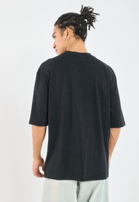 Svart t-skjorte med kort arm og avslappet passform, rund hals, myk tekstur og enkelt design, brukt sammen med lyse bukser.