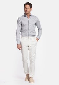 Lichtblauwe overhemden met een klein geometrisch patroon, gecombineerd met witte broek en lichtbruine instappers. Slim fit ontwerp.