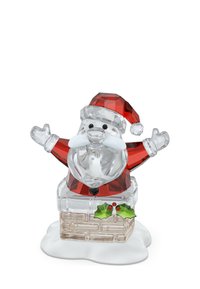 Figurita de cristal de Santa Claus con gorro y abrigo rojos, agitando las manos, emergiendo de una chimenea cubierta de nieve decorada con hojas de acebo.