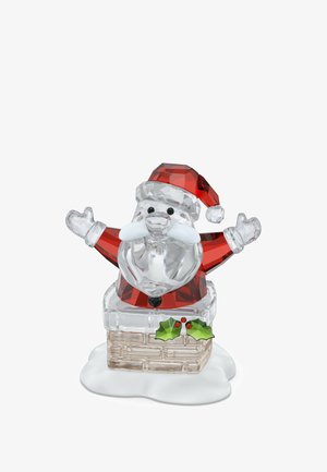 Figurina di cristallo di Babbo Natale con cappello e giacca rossi, che saluta con le mani, mentre emerge da un camino coperto di neve decorato con foglie di agrifoglio.