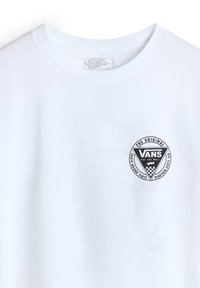 Camiseta de algodón blanca con un parche de logo negro de Vans que presenta un diseño triangular y acentos en forma de tablero de ajedrez en el lado izquierdo del pecho.