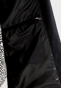 Intérieur noir d'une veste avec une poche zippée, texture lisse, et un extérieur contrastant blanc avec un motif zèbre.