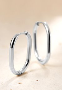 Srebrne kolczyki w kształcie wydłużonego owalu, z gładką, polerowaną powierzchnią i bezpiecznym zapięciem do mocowania.