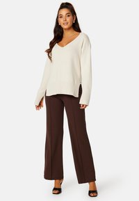 Maglione cremoso a collo a V con maniche lunghe abbinato a pantaloni a gamba larga marroni a vita alta. Tessuto liscio con vestibilità comoda.