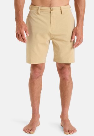 Shorts beiges en matière douce avec un devant plat, deux poches avant et une fermeture à bouton. Longueur mi-cuisses ; détails de design minimalistes.