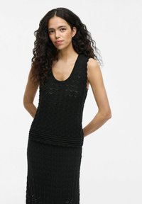 Vestido negro sin mangas con un patrón texturizado de zigzag, que presenta un corpiño ajustado y una cintura fruncida. Hecho de un material de punto ligero.