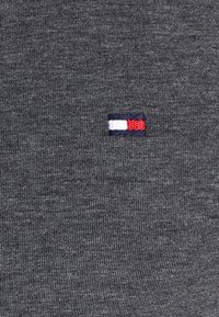 Tejido gris acanalado con un pequeño logotipo bordado rectangular que presenta franjas horizontales en blanco, rojo y azul marino.