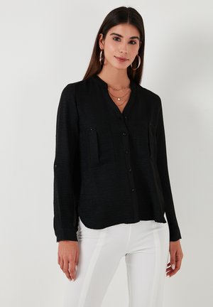 Black long-sleeve button-up shirt with a mandarin collar, two chest pockets, and a textured fabric. Paired with white pants.