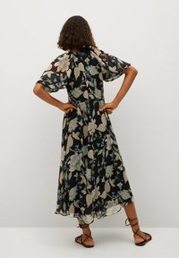 Robe noire fluide à fleurs avec de courtes manches bouffantes, ornée de fleurs pastel, taille cintrée et ourlet jusqu'aux chevilles. Sandales à lanières visibles.