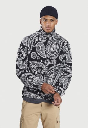 Black and white paisley-patterned fleece jacket with a high collar and zip front. Fabric appears soft with a textured surface.