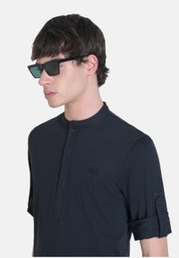 Camicia henley a maniche lunghe blu navy con polsini arrotolabili, dotata di una piastra con bottoni e un logo ricamato sul lato sinistro del petto.