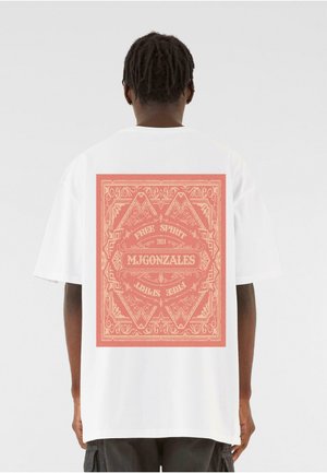 White cotton t-shirt featuring a large red graphic design on the back, with the text "FREE SPIRIT 2024 MJGONZALES" and decorative patterns.
