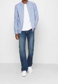 Světlomodrá košile s knoflíky a dlouhými rukávy, doplněná bílým tričkem a tmavě modrými džínami. Kombinováno s bílými teniskami, ležérní střih.