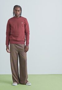 Bordeaux genser med ribbestrikkede mansjetter, kombinert med vide rutete bukser i brune og ferskenfargetoner. Lyse sneakers fullfører antrekket.