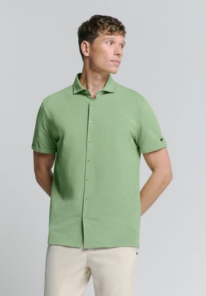 Korte mouw groene blouse met knopen in een lichte stof met een opgestikte kraag en subtiele textuur, gecombineerd met lichte broek.
