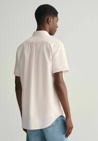 Camicia a maniche corte di colore rosa chiaro con un sottile motivo a quadri. La camicia è dotata di colletto classico e orlo curvo, realizzata in tessuto leggero.