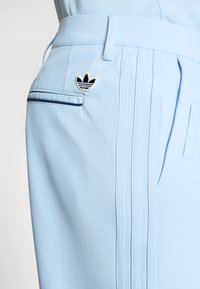 Jasnoniebieskie spodenki sportowe z tkaniny, z małym czarno-białym logo, bocznymi kieszeniami i detalami w paski.