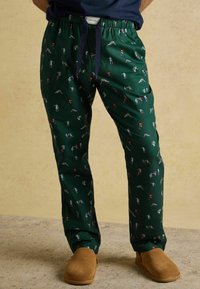 Zaļas pidžamu bikses ar rotaļīgu mazu figūru rakstu, kurām ir elastīga jostasvieta un tumši zilas šnīres. Mīksta auduma tekstūra.