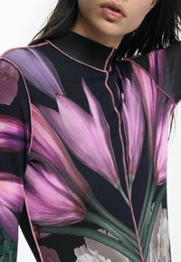 Lillemustriga pluus, millel on suured lillaõied mustal taustal, kõrge krae, keerukas roosa õmblus ja sile pind.