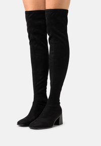 Zwarte suède over-de-knie laarzen met een puntige neus en een brede hak. Gladde textuur en eenvoudig ontwerp, reikend tot halverwege de bovenbenen.