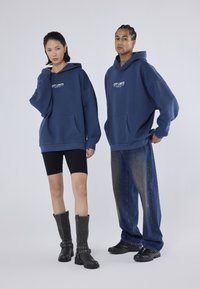 Námornícke oversized mikiny s prednými vreckami, čierne bikerské šortky a kontrastné čierne vysoké čižmy po kolená. Džínsy s vyblednutým dizajnom.