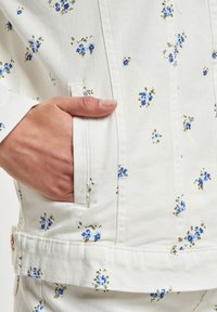 Blomstermønstret denimjakk i hvit med blå og grønne blomster, med sidelommer og et robust stoff.