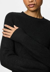 Maglione nero lavorato a maglia con texture a coste, colletto rotondo e maniche lunghe. Il tessuto appare morbido e caldo. Nessun motivo o decorazione visibile.
