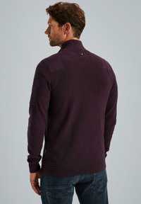 Dunkellila gestrickter Pullover mit hohem Kragen, gerippter Textur, seitlicher Tasche und horizontalen Rippen am Saum. Rückansicht dargestellt.