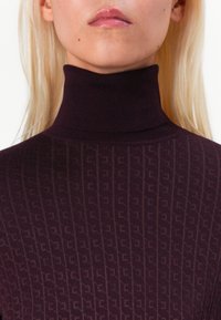 Dark purple turtleneck sweater featuring a ribbed texture and a subtle logo pattern throughout. Close-fitting design emphasizes silhouette.