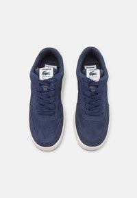 Baskets en daim bleu marine avec une texture lisse, semelle en caoutchouc, orteil perforé et lacets plats ; présente une étiquette de logo sur la languette et une semelle blanche contrastante.