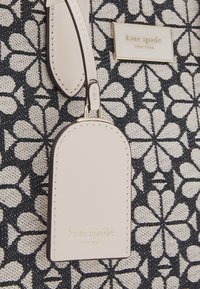 Borsa a tote in tessuto con motivo floreale nero, dettagli in pelle crema e una placca con logo dorato. Presenta un'etichetta beige con cuciture delicate.