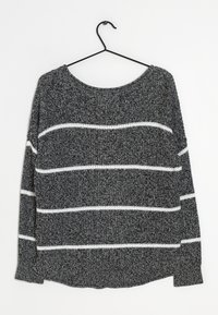 Mörkgrå stickad tröja med vita horisontella ränder hängande på en svart trådgalge mot en vit bakgrund.