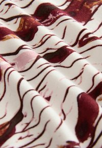 Strikket stof med bølgede maroon og lyserøde mønstre på en hvid baggrund, der har en blød tekstur og en subtil glans.