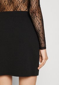 Svart figurnära klänning med genomskinliga spetslånga ärmar med ett blommönster. Slät tyg på klänningens del, som slutar strax ovanför knäet.