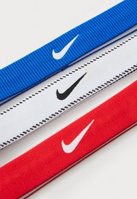 Trois élastiques en bleu, blanc et rouge, arborant le logo Nike. L'élastique bleu présente un motif rayé horizontal, tandis que les autres ont des textures lisses.