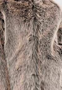 Tessuto in pelliccia sintetica nelle tonalità di grigio e nei colori pastello smorzati, caratterizzato da una texture lunga e soffice con una leggera sfumatura e variazioni di pattern naturali.