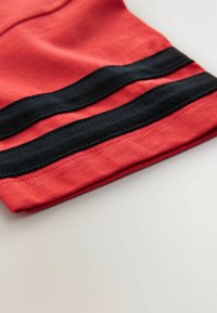 Tela de algodón roja con rayas negras horizontales cerca del dobladillo. La textura parece suave, con bordes cosidos para mayor durabilidad.