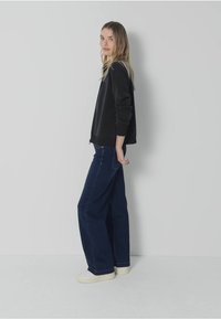 Czarny sweatshirt i granatowe szerokie dżinsy z jasnymi trampkami, pozujące na neutralnym tle, przedstawiające swobodny, miejski styl.