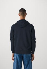 Felpa con cappuccio navy dal taglio morbido, con polsini a costine e una trama semplice, abbinata a jeans cargo azzurri chiari.