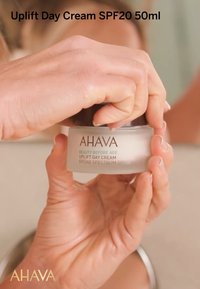 Crème de jour AHAVA Uplift, 50ml, dans un pot en verre givré avec un couvercle en argent. L'étiquette indique "Beauté avant l'âge" et "Protection solaire à large spectre SPF 20."